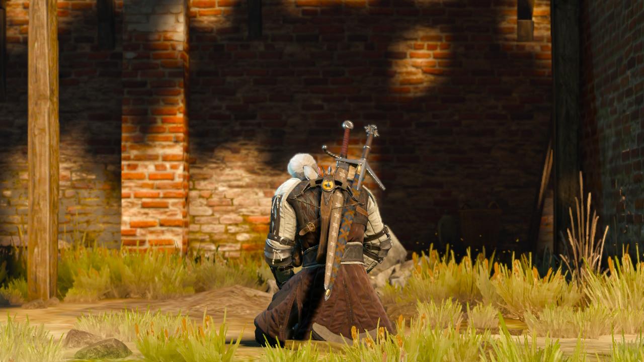 This is a picture of Geralt of Rivia kneeling down on the ground. He has white hair and is wearing brown and white leather armor. He also has a crossbow and two swords on his back, and around him is the grassy ground and a red brick building in the distance.